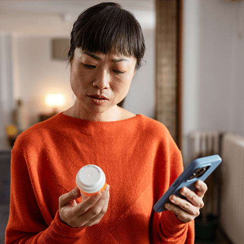 Woman looking at the pill bottle and holding phone